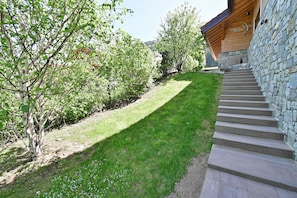Un escalier en pierre mène à un bâtiment en bois, qui est entouré d’une pelouse bien entretenue et d’arbres.