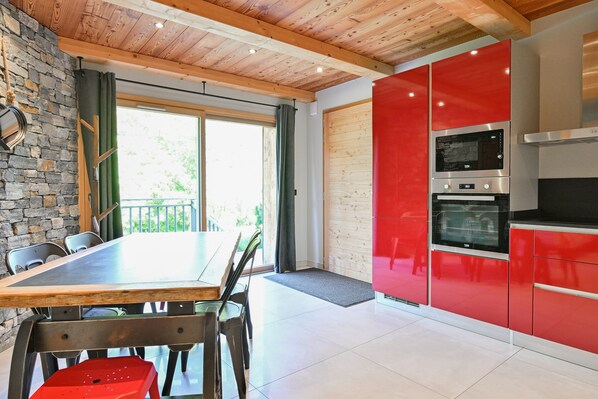 A modern kitchen with red cabinets, a wooden ceiling, and a dining area with a table and chairs.