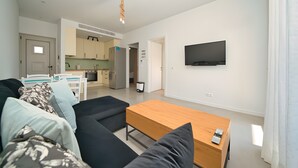 Un espace de vie moderne comprenant un canapé, une table en bois, un téléviseur et un coin cuisine.