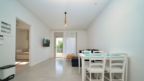 Une pièce moderne et bien éclairée, avec une table et des chaises, un téléviseur et une vue sur l’extérieur.