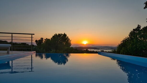 Une piscine avec vue sur le coucher de soleil, une rambarde et des arbres.