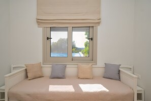 A bed with a view of a body of water and greenery through a window with a beige curtain. - Heli View Apartment with Sea View, Wi-Fi and Air Conditioning (Ermionida)