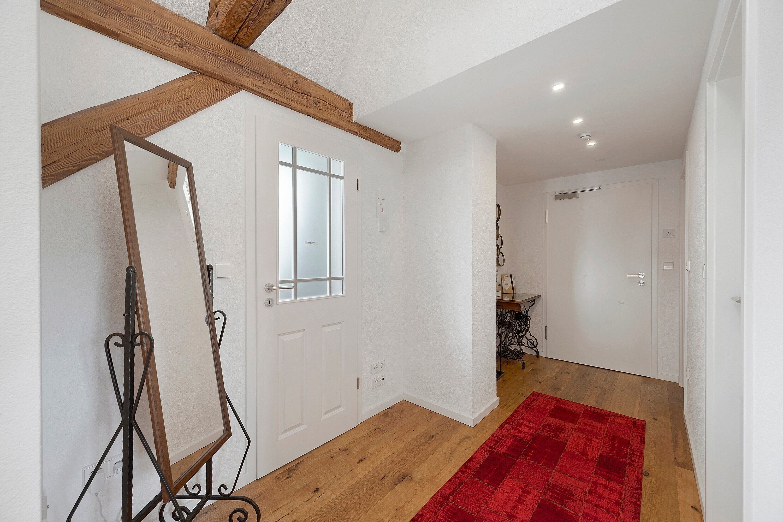 A room with wooden beams, a white door, a red rug, and a white wall.