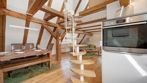 Zona pranzo con tavolo e panche in legno, una scala a chiocciola e una cucina con forno a incasso.