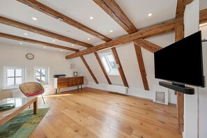A spacious loft with exposed wooden beams, a large flat-screen TV, and a dining area with a chair and table. - Historic Accommodation in Lorch (Lorch)