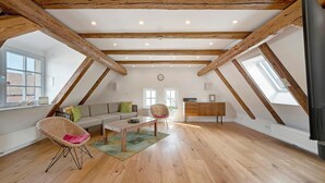 Une chambre mansardée avec des poutres en bois, un canapé, une chaise, une table et un téléviseur.
