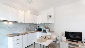 Ett modernt kök med vita skåp, en väggbeklädnad av marmor, ett matbord med stolar, en TV och en kaffemaskin.