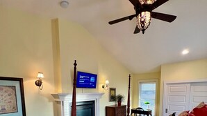 A bedroom with a four-poster bed, a ceiling fan, a fireplace, and a television on the wall. - The Judge's Chambers: Superior King Bed (Prescott)