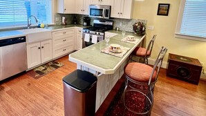 A modern kitchen with white cabinets, a central island, stainless steel appliances, and a bar stool. - The Judge's Chambers: Superior King Bed (Prescott)