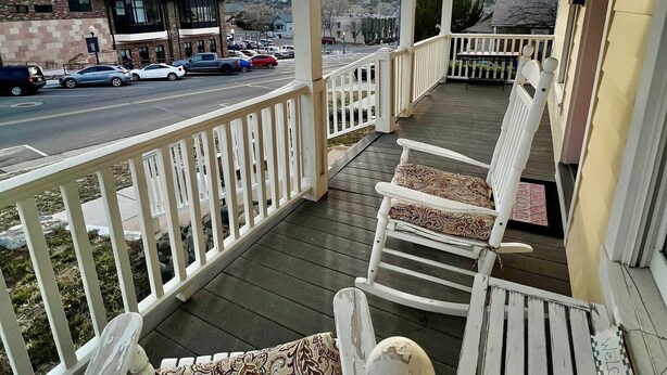 A porch with white railings and rocking chairs, overlooking a street with parked cars and buildings. - The Judge's Chambers: Superior King Bed (Prescott)