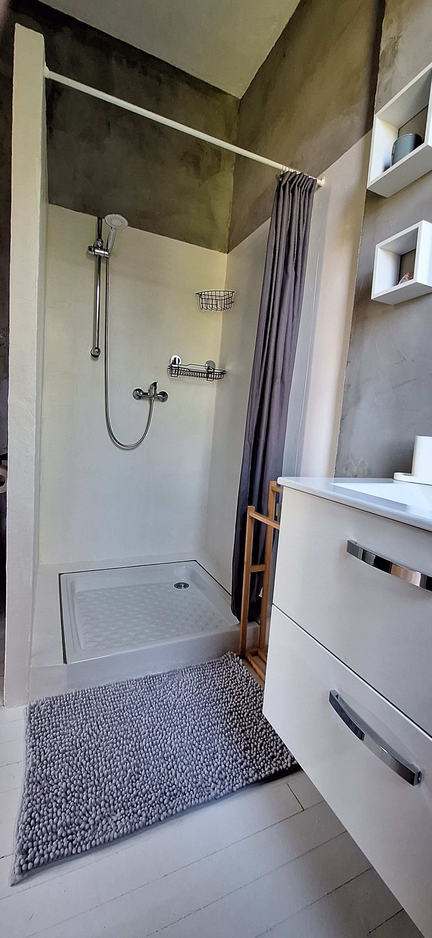 A modern bathroom with a shower, a sink, and a storage cabinet.