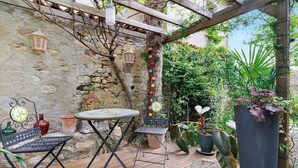 Un patio rústico al aire libre con una pérgola de madera, una pared de piedra y plantas en macetas.
