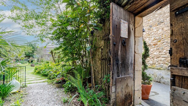 Una rústica puerta de madera con un letrero, un camino de grava y abundante vegetación.