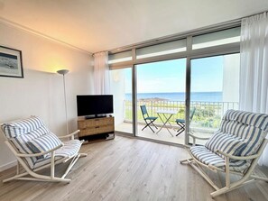 Un balcón con televisión, dos mecedoras a rayas y un mueble de madera.