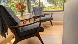 Two wooden chairs with grey upholstery and patterned throw blankets, positioned near a window with a view of greenery and flowers. - wyeangta - Woodbridge Waterfront Retreat (Woodbridge)