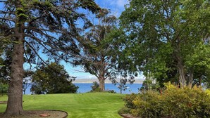 A well-maintained lawn with a curved pathway, mature trees, and a view of a body of water.