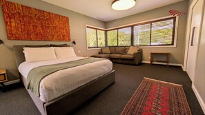 Una camera da letto con un letto grande, un divano, una finestra con tende, un tappeto e un quadro appeso al muro.