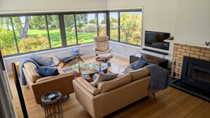 A spacious living room with a large window, a fireplace, a television, and a comfortable seating area.