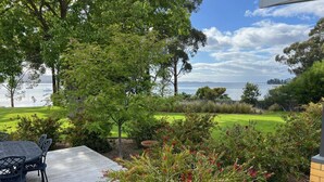 A patio with a table and chairs, surrounded by lush greenery and a view of a lake and distant hills.
