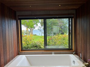 Un baño con una bañera grande, paredes de madera y una ventana con vistas a un jardín.
