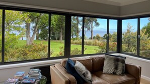 A room with a large window offering a view of a garden and the sea.