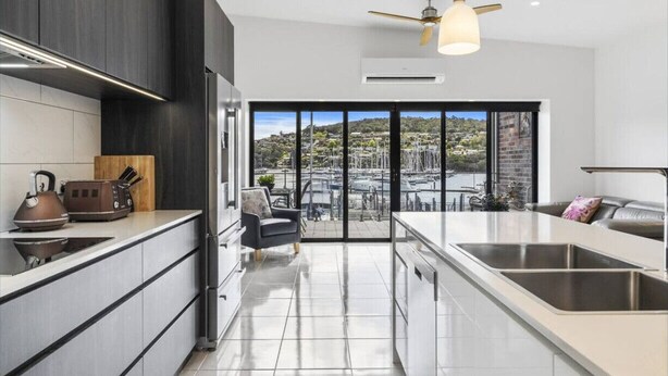 Una cocina moderna con una isla grande, muebles oscuros y vistas a un puerto deportivo a través de ventanas amplias.