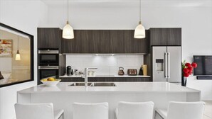 Una cocina moderna con una isla central, taburetes de bar, un refrigerador y una cafetera.
