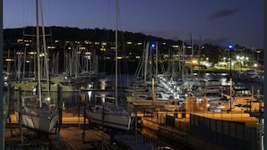 Una marina de noche con varias embarcaciones amarradas, rodeada de edificios iluminados.