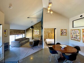 A modern interior with a dining area, a sofa, a bed, and artwork on the walls. - Glass Workshop: Industrial Apartment Urban Living (Hobart)
