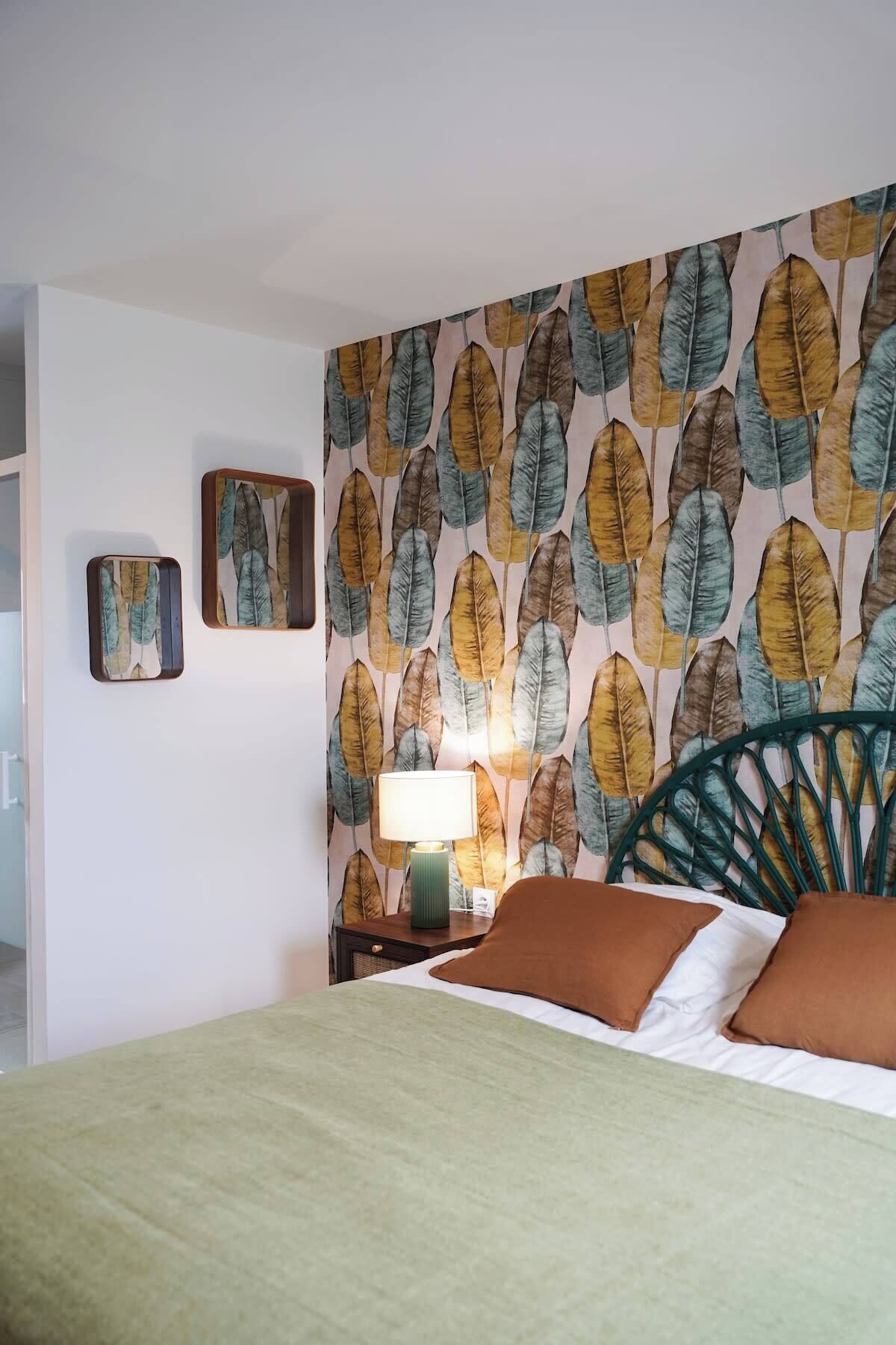 A bedroom with a bed, a nightstand with a lamp, and a wall with a leaf pattern.