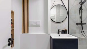 Une salle de bain moderne avec un lavabo blanc, un meuble-lavabo foncé, un panneau en bois, un miroir et une douche.
