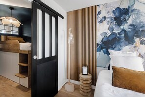 A modern bedroom with a bed, a wooden sideboard, a large floral wall mural, and a unique wooden stool with a lamp. - Horizon bleu depuis un studio unique (Carnac)