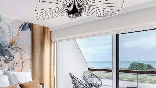Une chambre d’hôtel moderne dotée d’un grand lit, offrant une vue sur la mer et comprenant un balcon avec des chaises.