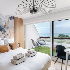 Une chambre d’hôtel moderne dotée d’un grand lit, offrant une vue sur la mer et comprenant un balcon avec des chaises.