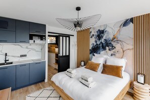 Une chambre d’hôtel moderne dotée d’une cuisine, d’un grand lit avec du linge de lit blanc et d’une grande œuvre d’art florale accrochée au mur.