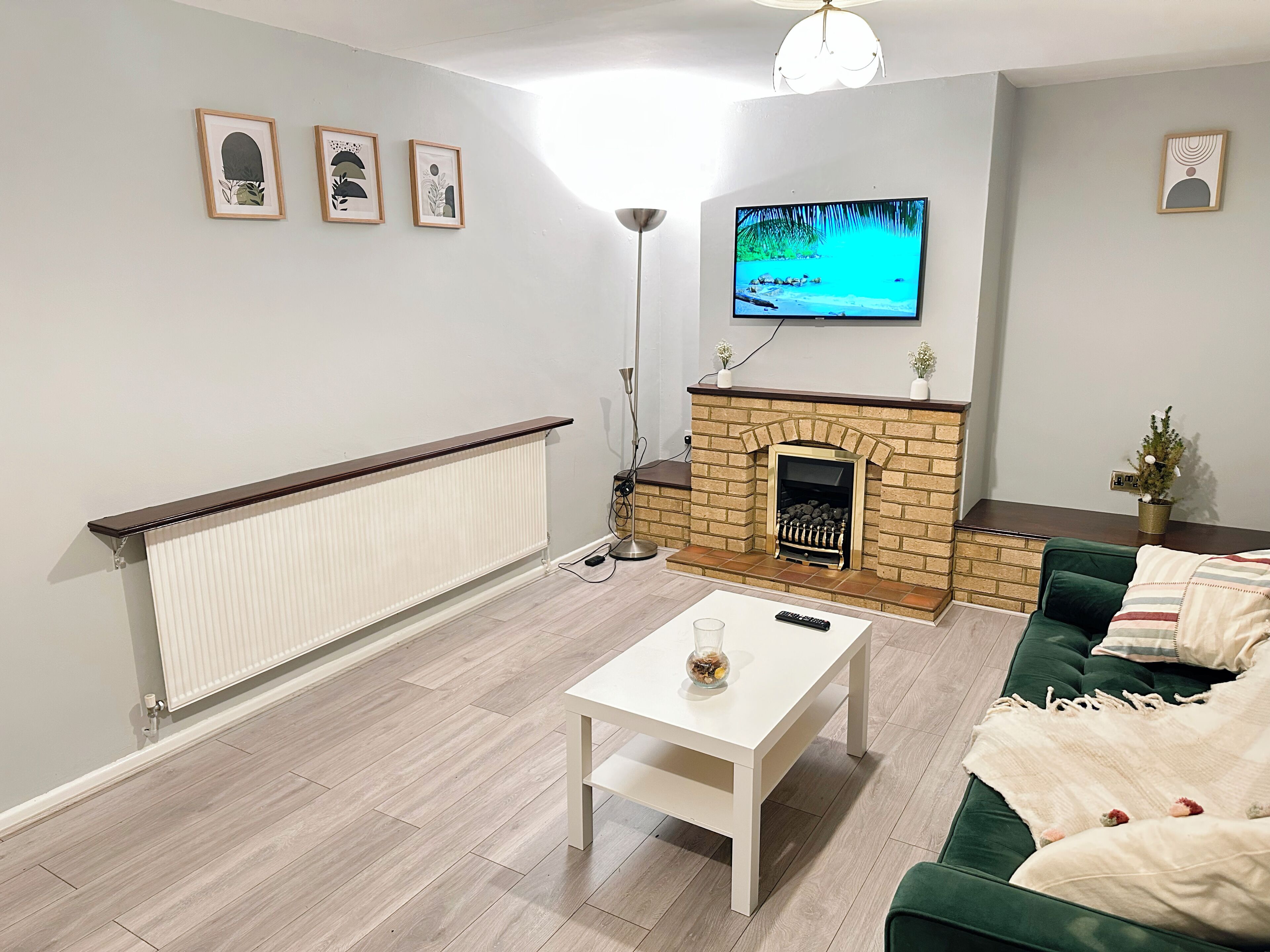 A living room with a fireplace, a television mounted above it, a green sofa, and a white coffee table.