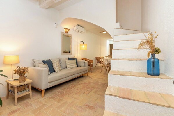 A living room with a sofa, a lamp, a vase with dried plants, and a staircase. - Casa con encanto a pie de playa (Tamariu)
