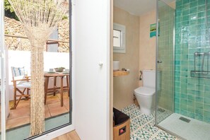 A bathroom with a toilet, shower, and a small sink. There is a glass door leading to a patio area with a table and chairs. - Casa con encanto a pie de playa (Tamariu)