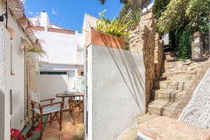 A courtyard with a table and chairs, a white wall, and a stone staircase. - Casa con encanto a pie de playa (Tamariu)