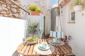 A wooden table with two cups and a bowl of fruit, set against a white wall with a stone base. - Casa con encanto a pie de playa (Tamariu)