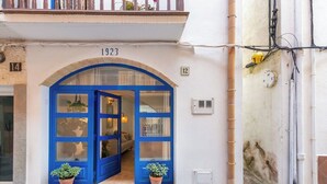Un edificio con un ingresso ad arco blu con la scritta "1923", piante in vaso all'ingresso e cavi elettrici a vista.