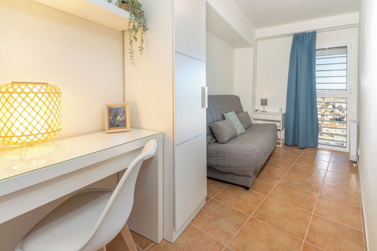 Un dormitorio moderno con una cama, un escritorio con lámpara y vistas a la ciudad desde una ventana.