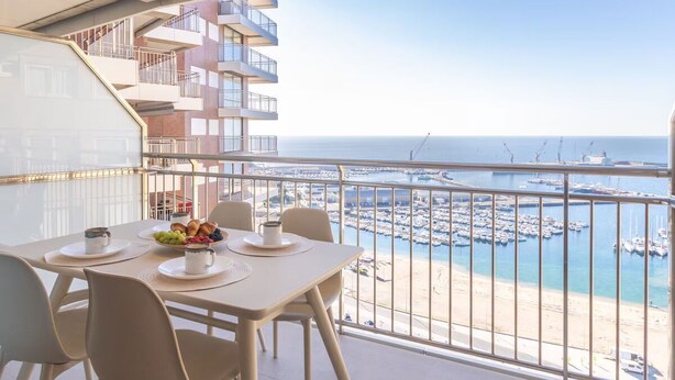 Ein Balkon mit Frühstückstisch, mit Blick auf einen Yachthafen und Strand.