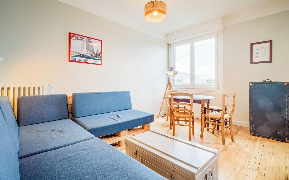 A compact living space with a blue sofa, a small dining table with chairs, a lamp, and a suitcase.