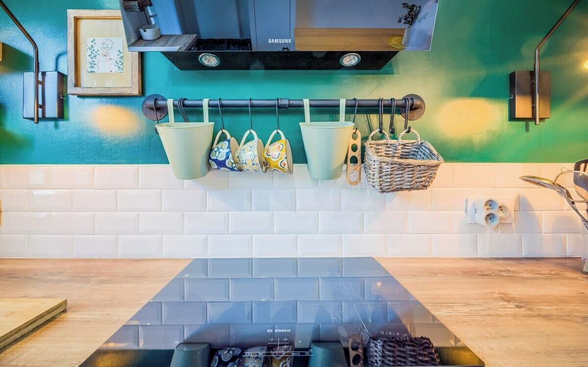 A kitchen with a Bosch induction cooktop, a hanging pot rack with various kitchen utensils, and a Samsung range hood.