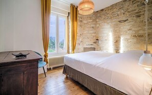 Ein Schlafzimmer mit einer Steinsäule, einem Holztisch, einem Bett mit weißer Bettwäsche und einem Fenster mit Vorhängen.