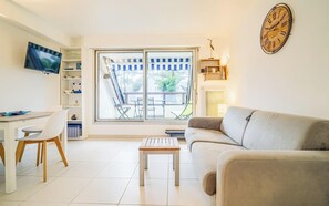 Una sala de estar con sofá, televisor montado en la pared, mesa de comedor con sillas y un ventanal con vistas al exterior.