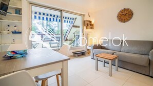A modern living room with a sofa, a dining table, and a staircase leading to a balcony. - Vacances à pied studio charmant à 1min des plages (Carnac)