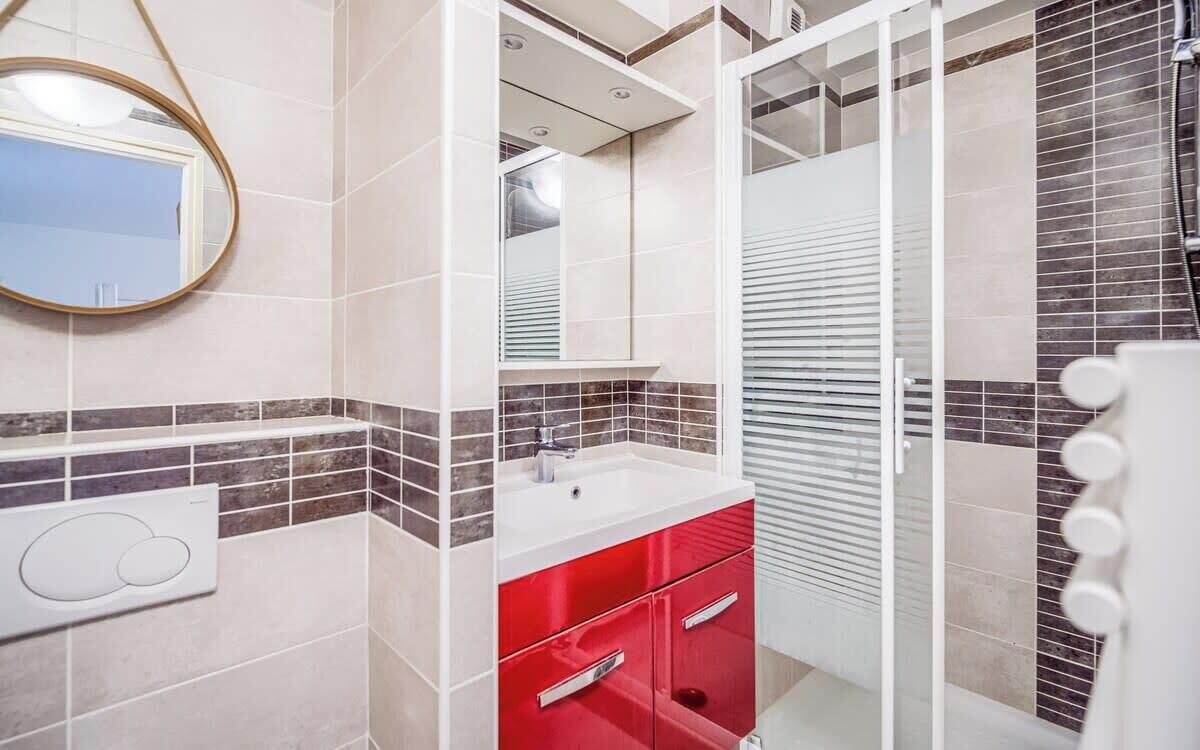 A modern bathroom with a white sink, red vanity, and a glass shower enclosure.