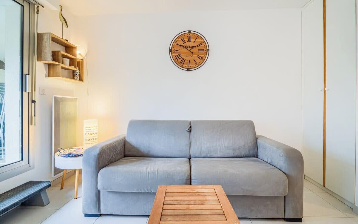 Een moderne woonkamer met een grijze bank, een houten salontafel, een wandklok en een boekenkast.